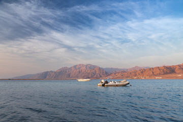 Sunny morning at sea shore with motor boat and mountain in background under light clouds Dahab Egypt