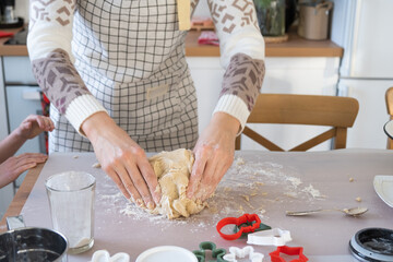 Obraz na płótnie Canvas Hands knead thick dough on the kitchen table, decorated with festive decorations for Christmas and New year. Baking at home, aroma and comfort. Close-up