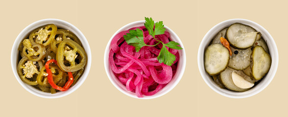 A pattern of pickled jalapeno peppers, red onions and cucumbers in white bowls on yellow...