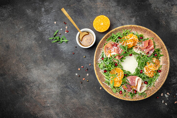 Fresh salad with mandarins, prosciutto jamon and Parmesan cheese on a dark background. Healthy...