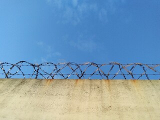 Barbed wire prison wall with blue sky background.
