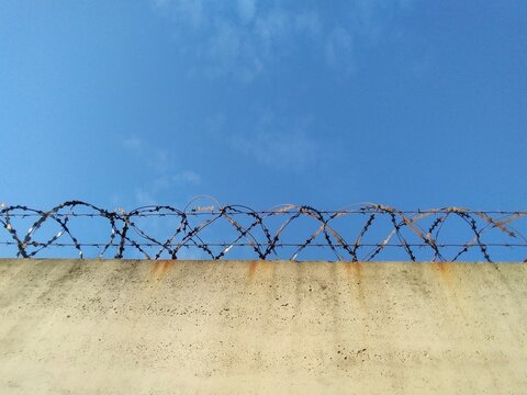Barbed wire prison wall with blue sky background.
