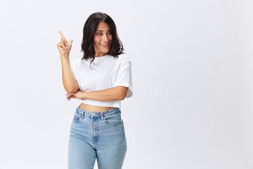 Woman in white t-shirt on white background brunette hands up gestures and signals poses in jeans emotion, lifestyle smiles, copy space