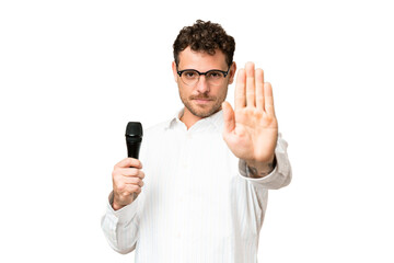 Brazilian man picking up a microphone over isolated chroma key background making stop gesture