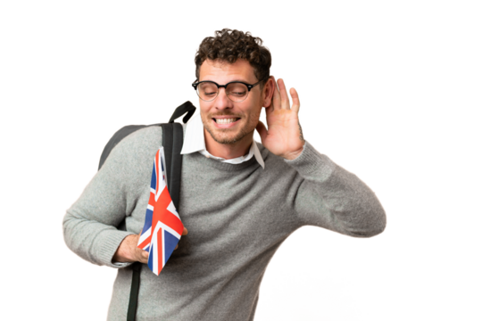 Brazilian man holding an United Kingdom flag over isolated chroma key background listening to something by putting hand on the ear