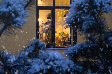 Cozy festive window of the house outside with the warm light of fairy lights garlands inside -...