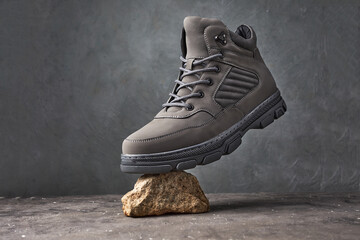 Male walking boots with stones or concrete block on gray background. Autumn stylish leather shoes...