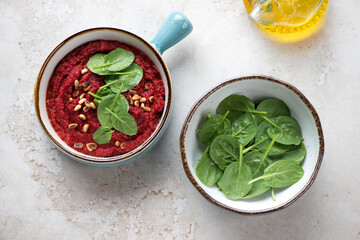 Turquoise bowls with beetroot caviar and fresh spinach leaves on a beige stone background, horizontal shot, high angle view