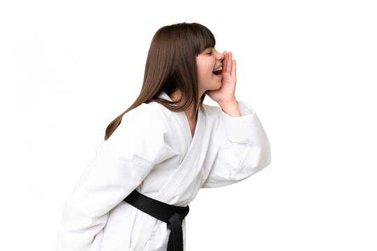 Little Caucasian girl doing karate over isolated background shouting with mouth wide open to the lateral