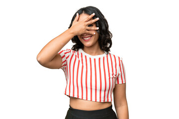 Young Argentinian woman over isolated background covering eyes by hands and smiling