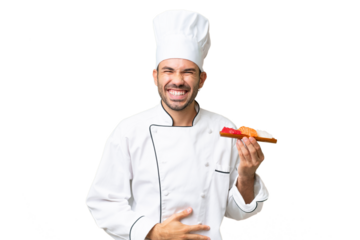 Young caucasian chef holding a sushi over isolated background smiling a lot