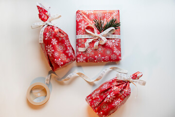 Christmas gifts wrapped in red paper on a white table with decorative elements next to them