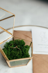 The concept of love and relationships. Wedding invitation. Gold rings in a gold casket on a marble table. Craft envelopes with invitations. Close-up.