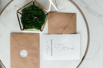 The concept of love and relationships. Wedding invitation. Gold rings in a gold casket on a marble table. Craft envelopes with invitations. Close-up.
