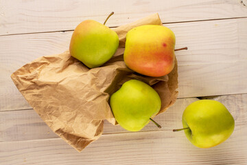 Several sweet green apples with paper bag on wooden table, macro, top view.