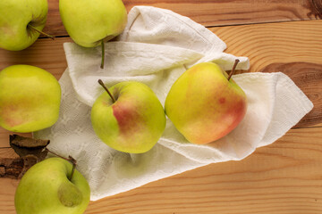 Several sweet green apples with white linen napkin on wooden table, macro, top view.
