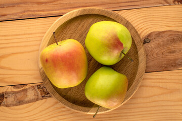 Three sweet green apples in a wooden plate on a wooden table, macro, top view.