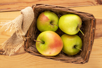 Several sweet green apples in a basket on a wooden table, macro, top view.
