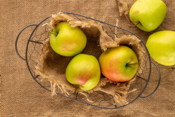 Several sweet green apples with basket on jute cloth, macro, top view.