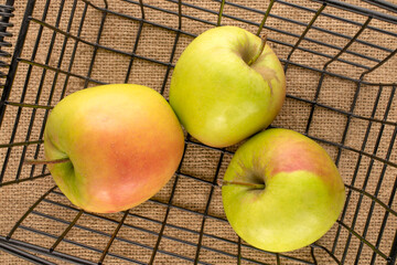 Three sweet green apples in a basket on a jute cloth, macro, top view.