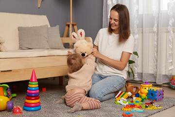 Portrait of happy mom and daughter playing, early education and development, loving family having fun together playing with plush soft toys at home on the floor.