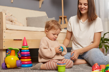 Young mother and little baby assembling plastic toys, method early development, confident family constructing toy tower use self educational game at home. - obrazy, fototapety, plakaty