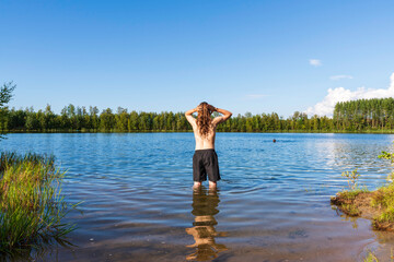 Young man with long hair takes a dip in a lake. Finland