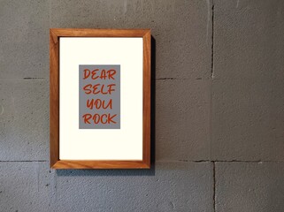 Photo frame on copy space gray wall with text DEAR SELF YOU ROCK, concept of positive self talk to...