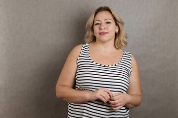 Close-up portrait of a blonde woman plus a size on a gray background, copy space, looks at the camera