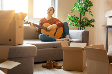 Woman sits on a sofa and plays the guitar in her new apartment. Concept of buying a new apartment...