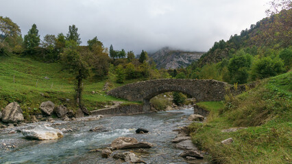 Old stone bridge at the path to the Cirque de Gavarnie on a cloudy autumn day, - obrazy, fototapety, plakaty