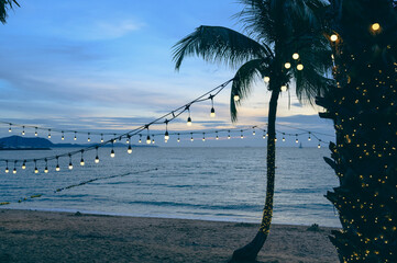 light bulbs on string wire decoration at the party event festival on the beach at sunset. Outdoor...