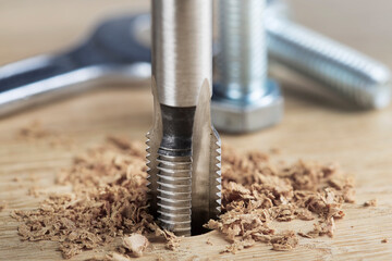 Thread tap drill cutting hole in wooden plate. Working cutter.