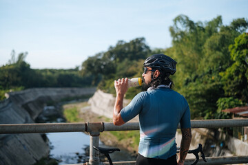 A young bearded cyclist drinking from a drinking bottle.