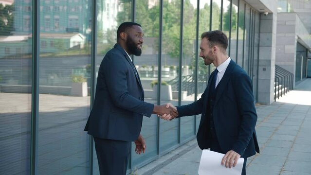Handshake of two male top managers in business suits standing in the business district. Two male top managers shake hands as a sign of a successful sale and a win-win deal. Business concept