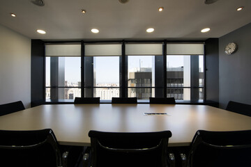 Boardroom with long wooden table with black swivel chairs and wall of windows with city views
