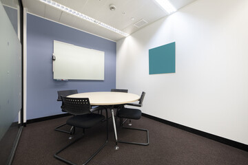 Boardroom with round white wooden table with black chairs and whiteboard with deleble markers
