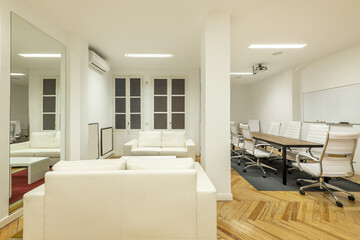 Office with white leather sofas, hardwood floors and a meeting table with white swivel chairs