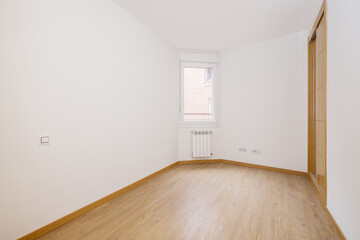 bedroom with a two-section built-in wardrobe with oak sliding doors in one corner and wooden floors and a window with a white aluminum radiator below