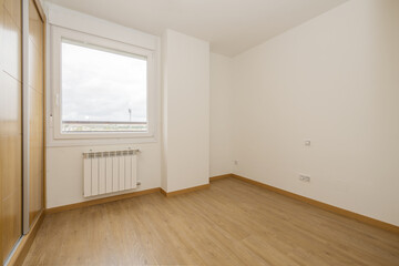 bedroom with a two-section built-in wardrobe with large oak sliding doors and wooden floors, a single-pane aluminum window with views and an aluminum radiator below