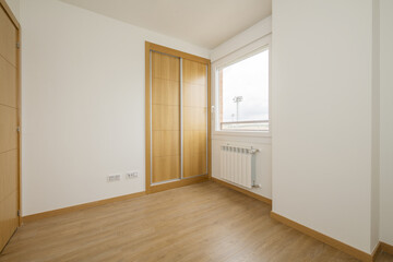 bedroom with a two-section built-in wardrobe with large oak sliding doors and wooden floors, a single-pane aluminum window with views, access doors of the same material and an aluminum radiator below