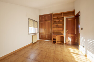 bedroom with built-in wardrobe with sapelly folding doors, skirting boards and interior doors of the same material and light brown stoneware floors