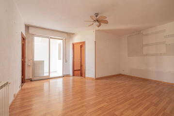 Empty living room with sapele wood interior doors with white painted walls, ceiling fan with wooden blades and enclosed terrace with aluminum and glass sliding doors