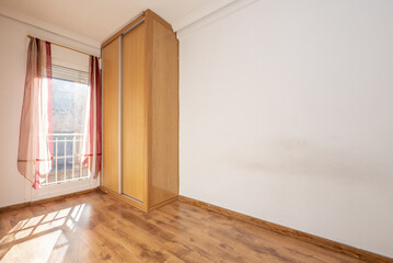 Empty room with a built-in wooden wardrobe with sliding doors with aluminum edges next to a window...