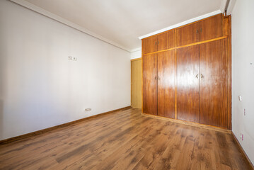Empty room with built-in wooden wardrobe with 4 sapele wood doors and laminated flooring