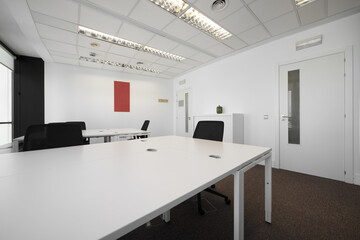 White and empty shared office desks in an office with carpeted floors and technical ceilings