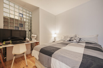 Bedroom with a double bed with pine wood flooring, a white desk with a PC next to a skylight wall...