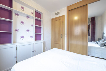 Bedroom with a double bed with a white wooden shelf with doors and a wardrobe with sliding mirror doors and oak wood