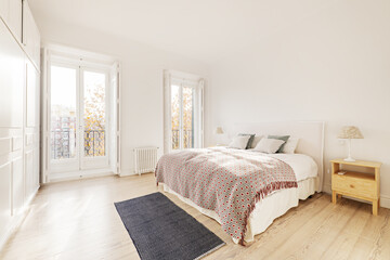 Double bedroom with a large bed, wooden bedside tables, large windows with balconies and white built-in wardrobes