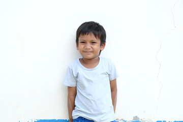 Portrait of cute little asian boy leaning against the white wall with smiley and funny face